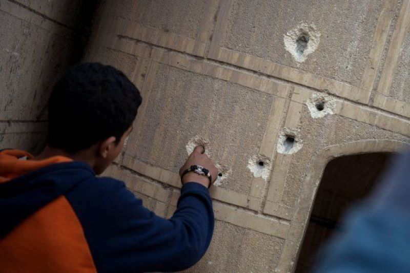 Un curioso mete el dedo en el agujero de uno de los impactos de bala en unmuro próximo a la iglesia Mar Mina tras el ataque.