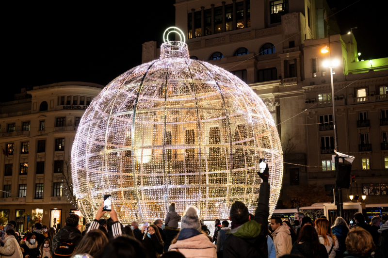 Una multitud de personas observan la bola de luz ubicada en la Plaza de España de Madrid.