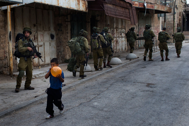 Un niño palestino infla un globo delante de soldados israelíes de patrulla por Hebrón, Cisjordania. 